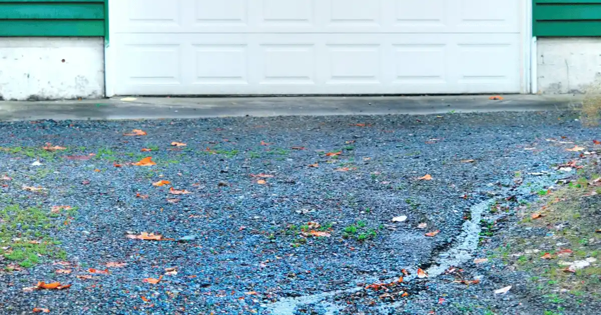 Damaged driveway surface with cracks, water, and worn pavement near a garage door.