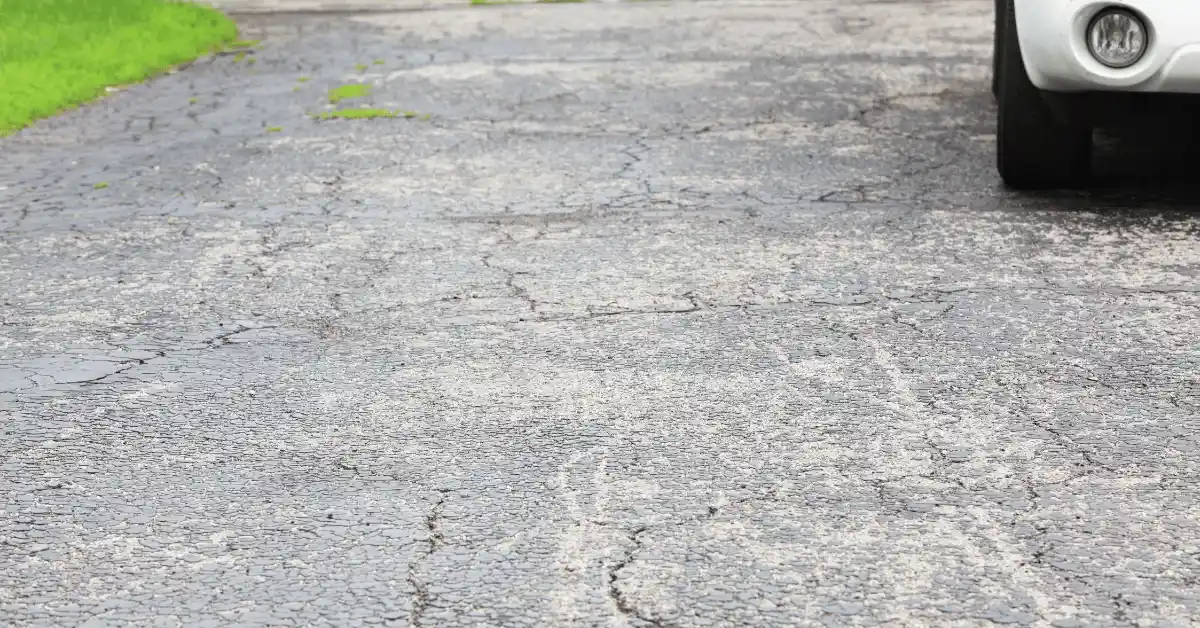 Close-up of a weathered, cracked driveway surface with a parked vehicle nearby.