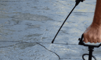 A person power washing a concrete surface using a handheld spray nozzle, demonstrating safe and effective techniques for cleaning concrete without causing damage.