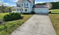 Cracked concrete driveway leading to a residential home with a two-car garage and front porch.