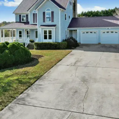 Cracked concrete driveway leading to a residential home with a two-car garage and front porch.