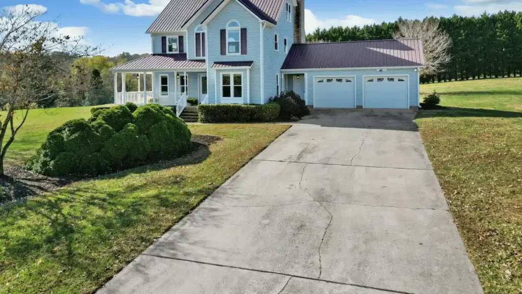 Cracked concrete driveway leading to a residential home with a two-car garage and front porch.