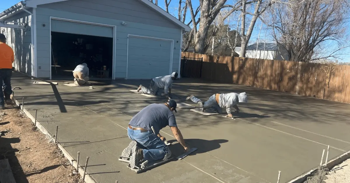 Concrete crew hand-troweling and finishing a fresh driveway pour outside a residential garage