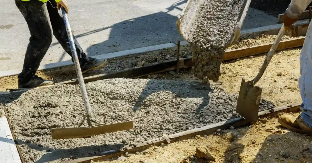 Workers raking and shoveling wet concrete as it pours from a chute into wood-framed forms