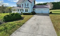 Cracked concrete driveway leading to a residential home with a two-car garage and front porch.