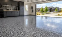 Finished epoxy garage floor with gray flake coating, glossy surface, storage cabinets, and open garage door in a Colorado neighborhood.