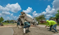 Concrete crew pouring and finishing a residential driveway from a ready mix truck, demonstrating professional concrete installation and proper finishing techniques.